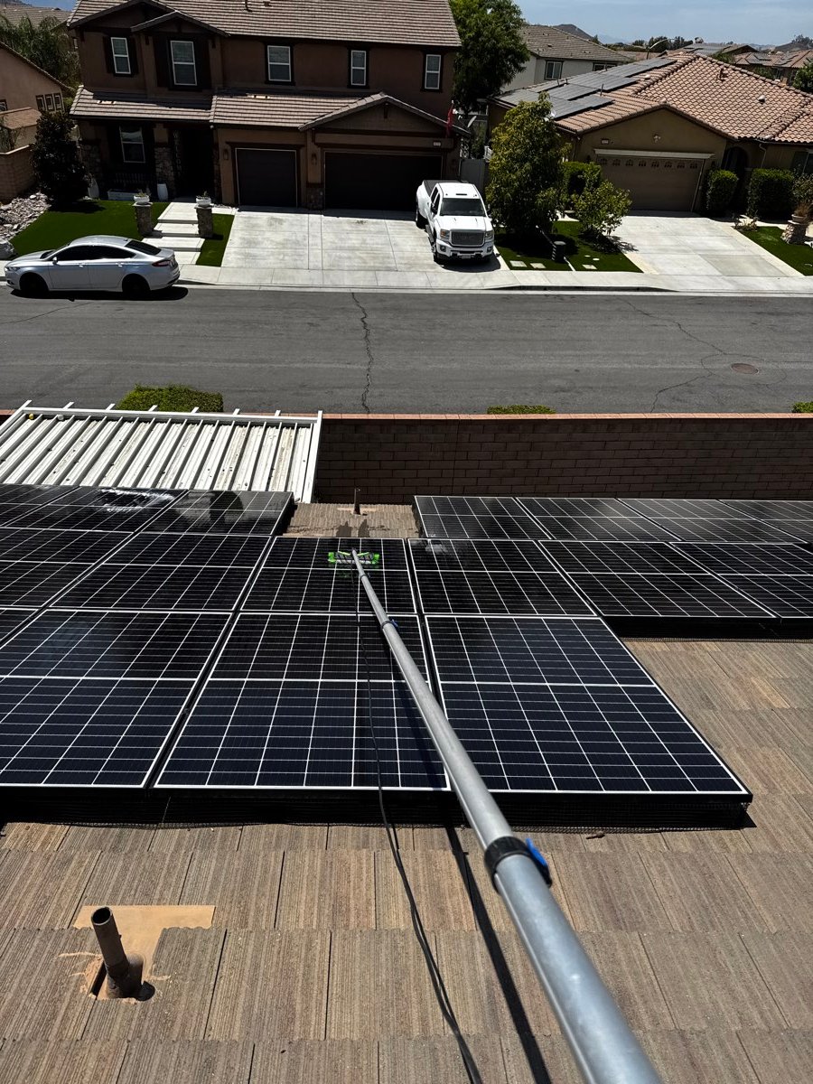 Technician cleaning a solar array with a water-fed pole, service truck parked below