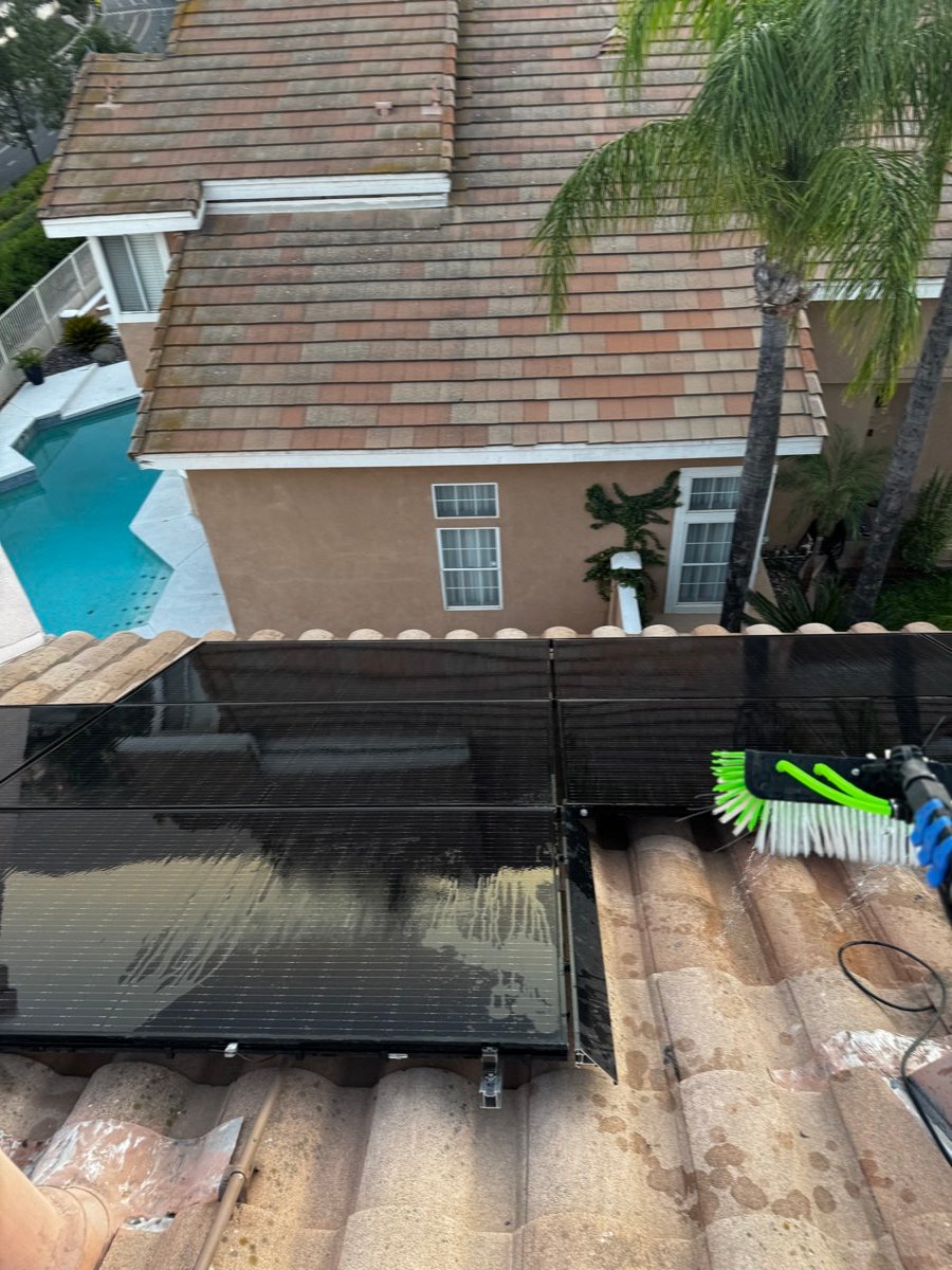 Brush cleaning a solar panel up close, backyard pool in the background