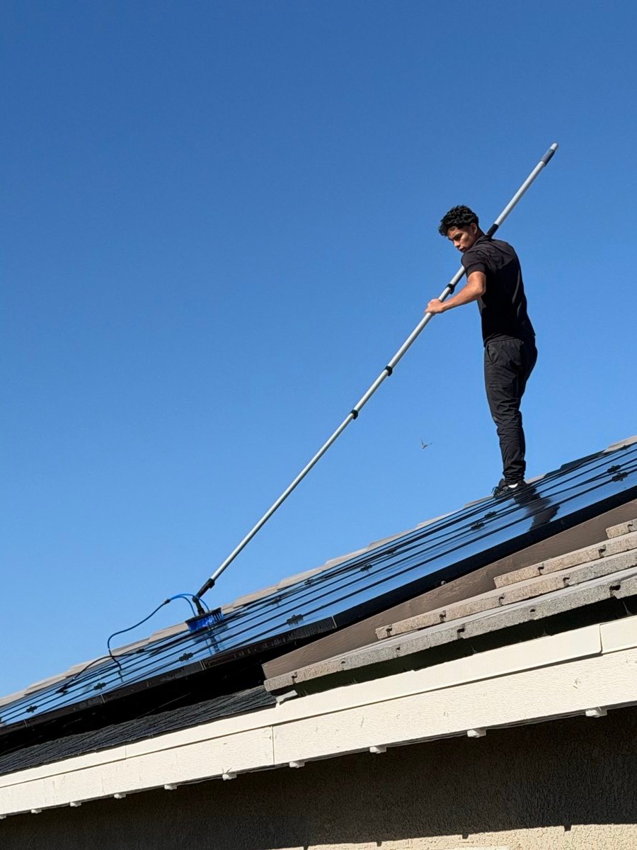 Technician reaching a second-story window with a water-fed pole against a blue sky