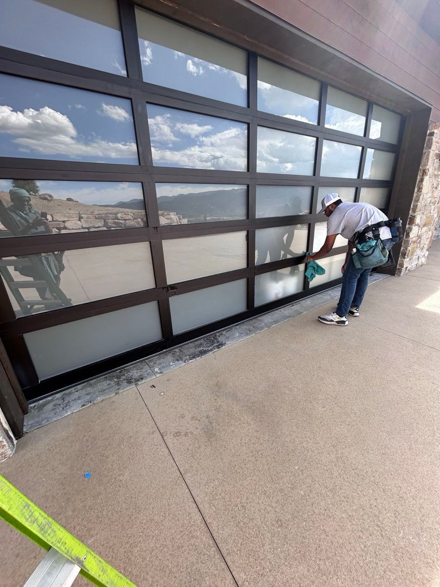 Technician cleaning a large glass garage-style door on a modern home